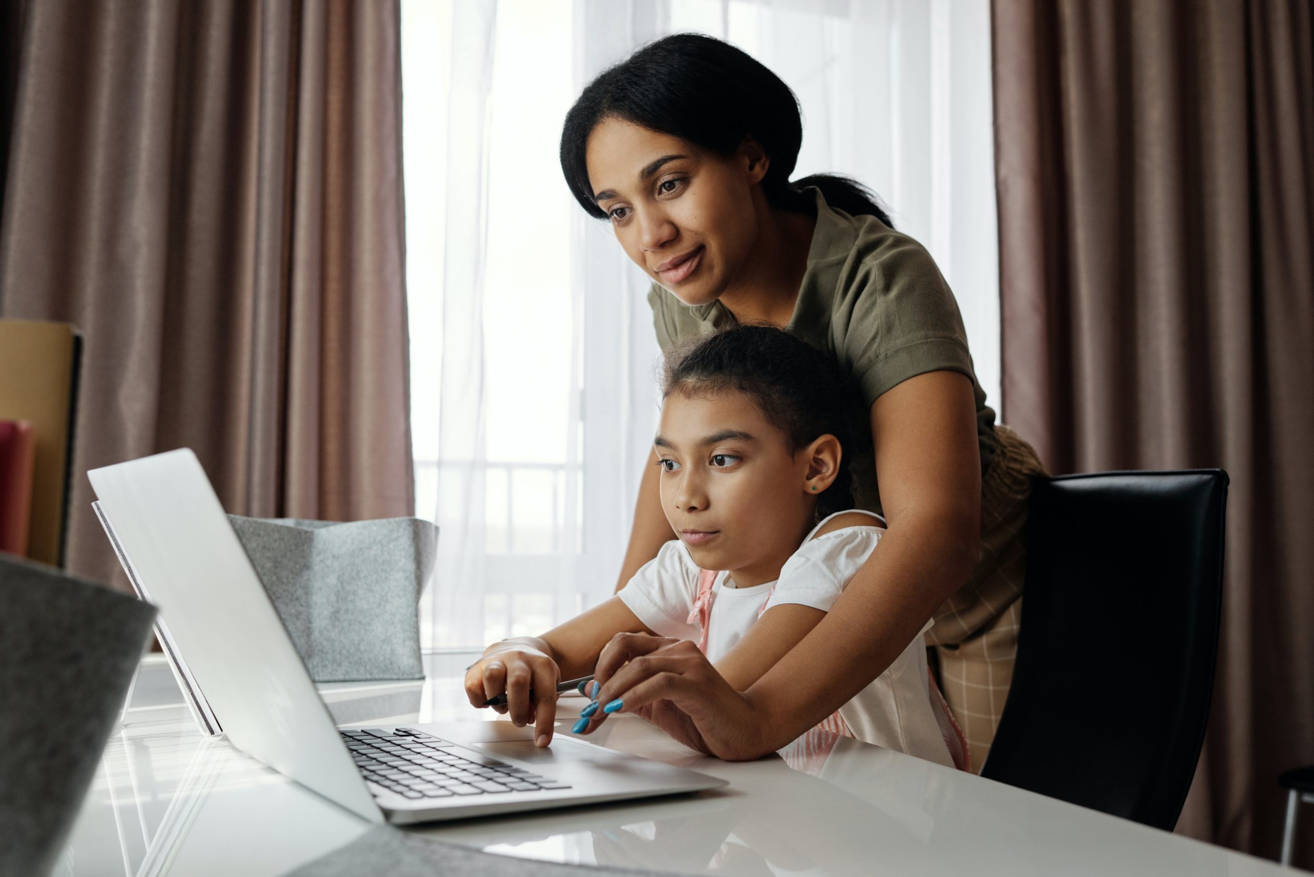 mother helping young daughter on laptop